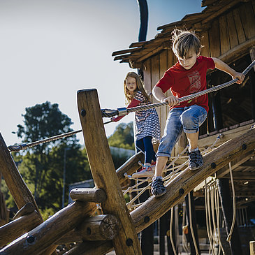 Das Bild zeigt zwei Kinder, die auf einem Klettergerüst eines Spielplatzes beim Freizeitzentrum Peterberg klettern.