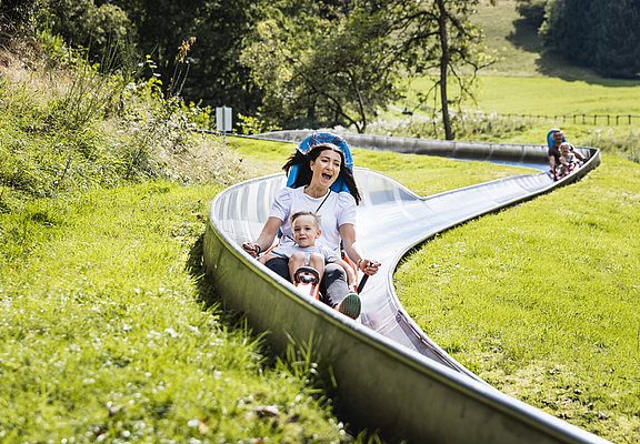 Das Bild zeigt eine Frau und einen Jungen, die die Sommerrodelbahn beim Freizeitzentrum Peterberg fahren.