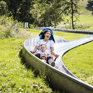 Das Bild zeigt eine Frau und einen Jungen, die die Sommerrodelbahn beim Freizeitzentrum Peterberg fahren.
