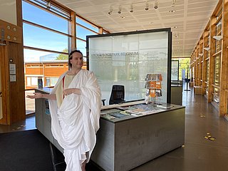 Das Bild zeigt eine römische Figur und die Dauerausstellung im Kulturzentrum Belginum Archäologiepark.