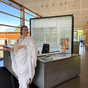 Das Bild zeigt eine römische Figur und die Dauerausstellung im Kulturzentrum Belginum Archäologiepark.