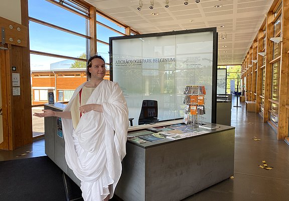 Das Bild zeigt eine römische Figur und die Dauerausstellung im Kulturzentrum Belginum Archäologiepark.