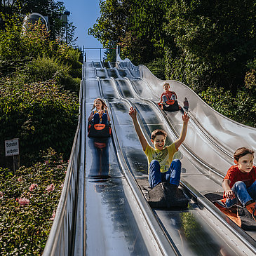 Das Bild zeigt mehrere Kinder, die die Teppichrutsche beim Freizeitzentrum Peterberg runterrutschen.