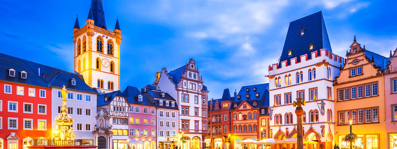 Das Bild zeigt einen alten Platz mit schön verzierten Häusern in Trier bei Abendstimmung- und beleuchtung.