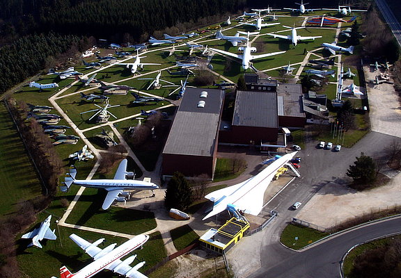 Das Bild zeigt eine Luftaufnahme vom Gelände der Flugausstellung Junior mit zahlreichen Flugzeugen und dem Hauptgebäude.