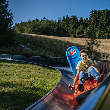 Das Bild zeigt einen Jungen, der die Sommerrodelbahn beim Freizeitzentrum Peterberg fährt.
